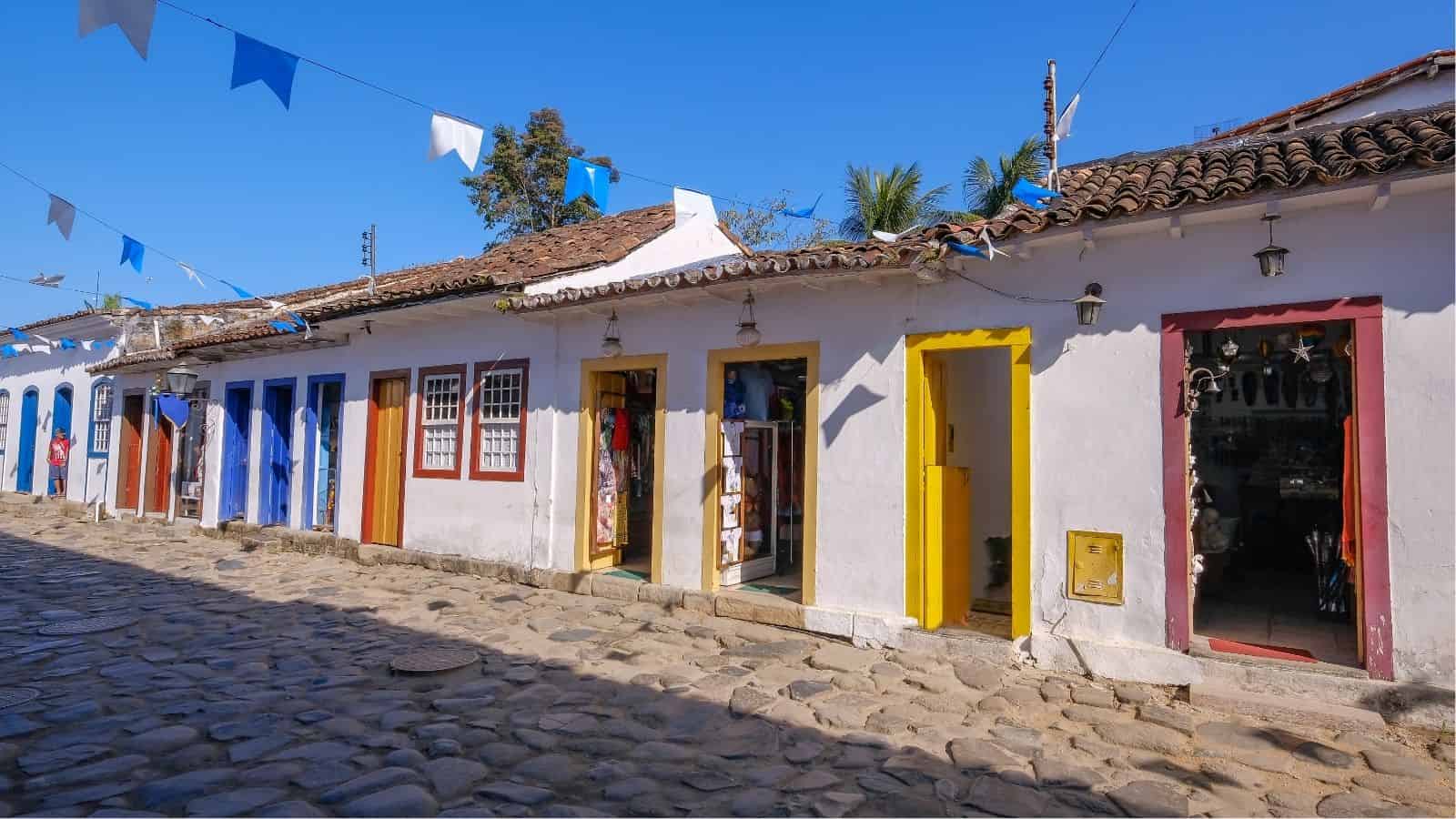 Colorful doors on a cobblestone street with festive flags and white colonial-style buildings under a blue sky.