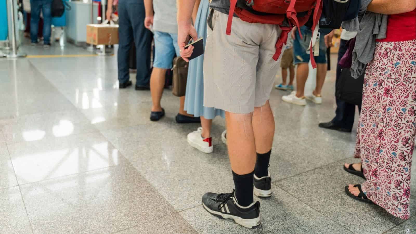 People standing in line at an airport, visible from the waist down on a shiny floor.