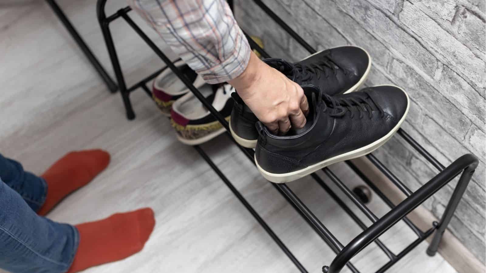 A person places black sneakers on a shoe rack next to a pair of red socks and other shoes.