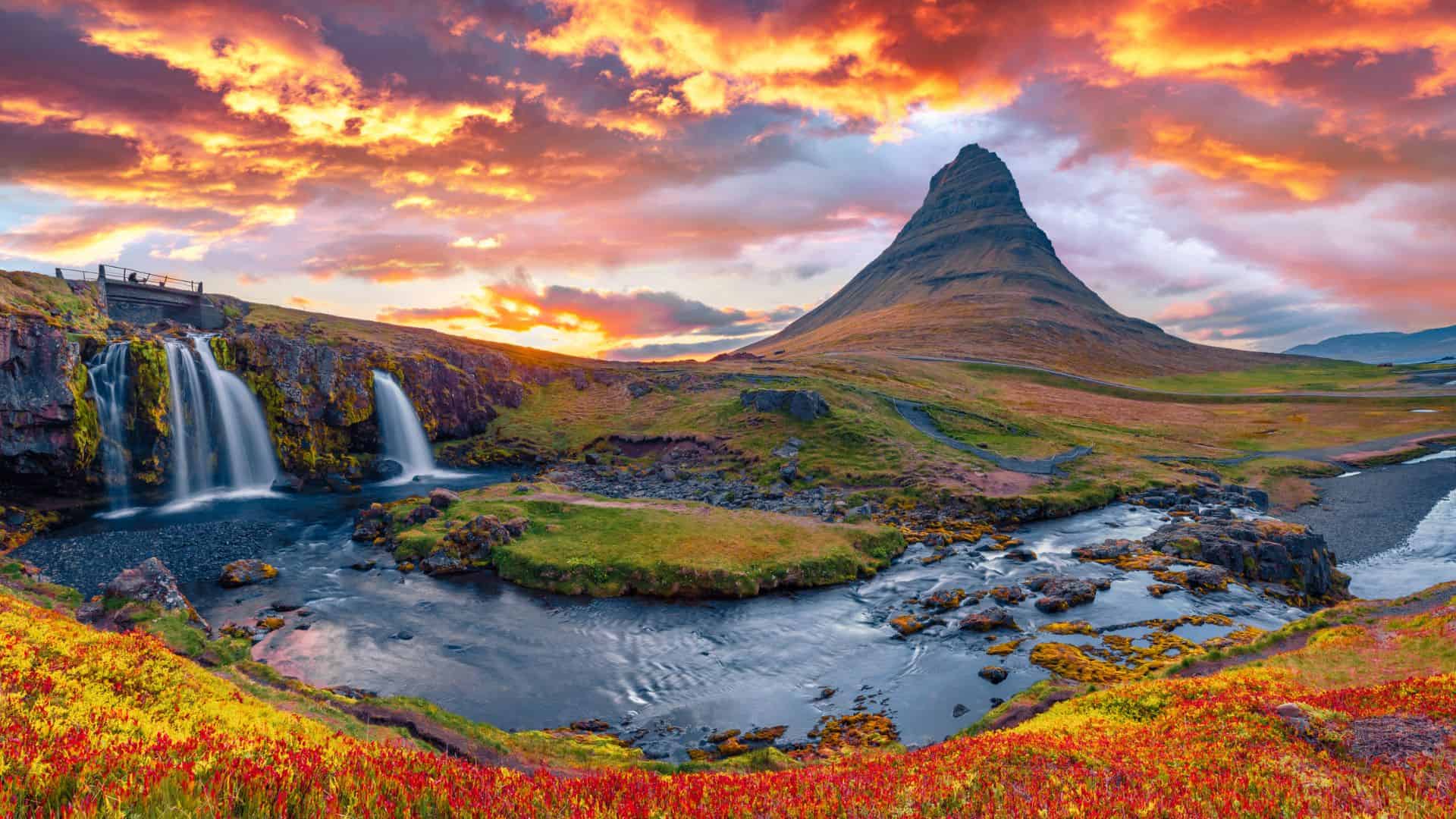 A vibrant sunset over Kirkjufell mountain, a waterfall, and colorful fields in Iceland.