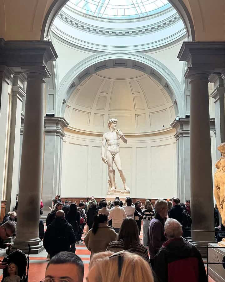 Crowd admiring Michelangelo's David statue in a grand, domed gallery with natural light&mdash;a must-see highlight on any Florence Italy itinerary.