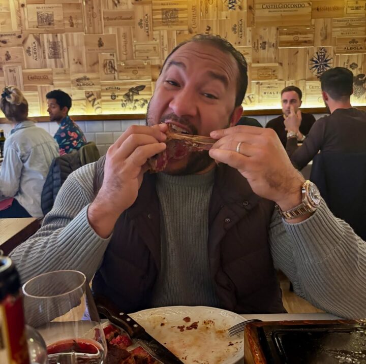 A man in a restaurant enthusiastically eating meat off a bone with both hands, savoring the rich flavors of authentic Florence food.