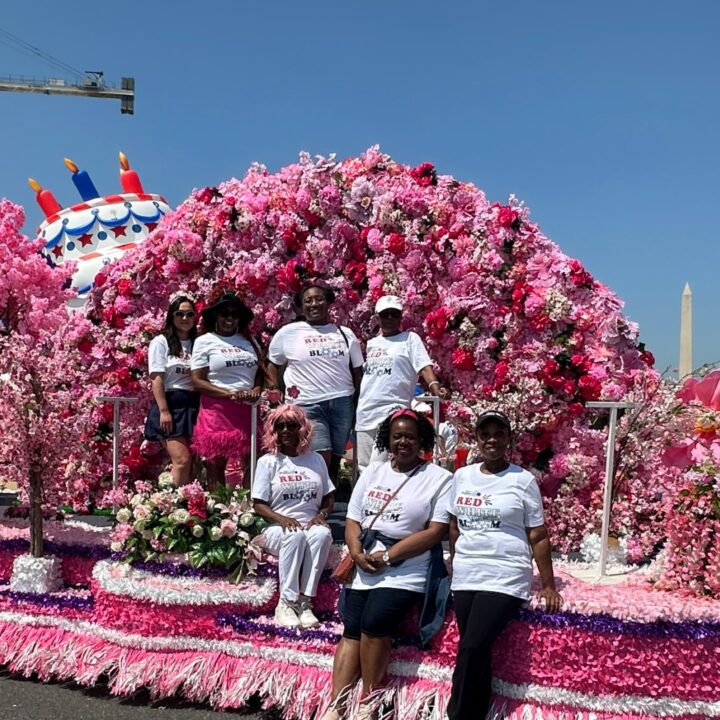 Seven women in matching shirts pose on a parade float covered in pink flowers, with the Washington Monument behind&mdash;celebrating one of the best festivals for world travel enthusiasts.