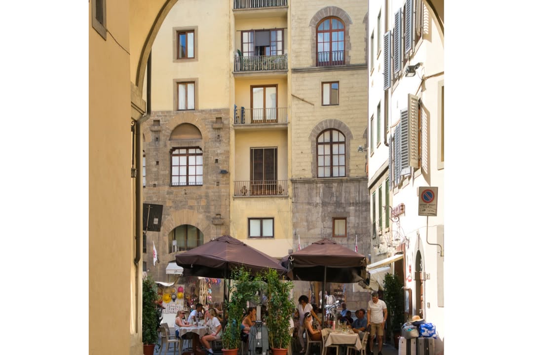 Outdoor caf&eacute; with people sitting at tables under umbrellas, set against old European-style buildings&mdash;an ideal stop on any Florence Italy itinerary.