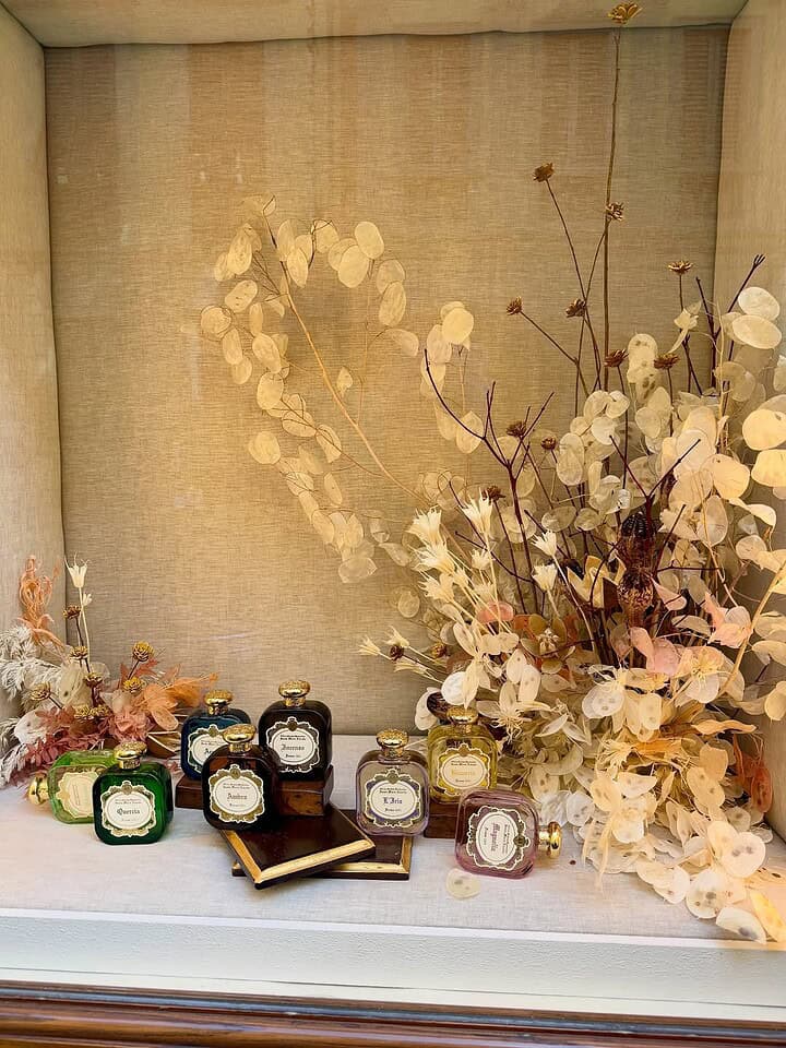 Perfume bottles displayed with dried flowers and books in a beige, softly lit window display&mdash;perfect inspiration for your Florence Italy itinerary.