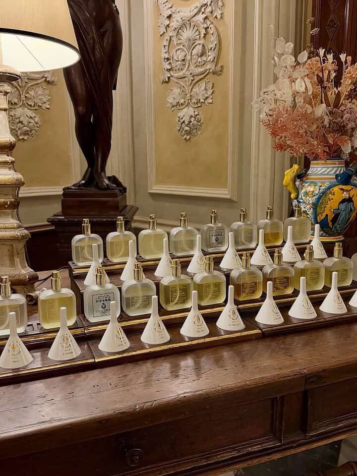 Perfume bottles arranged neatly on a wooden table in an ornate, elegant room with floral decorations&mdash;reminiscent of a stop on a Florence Italy itinerary.