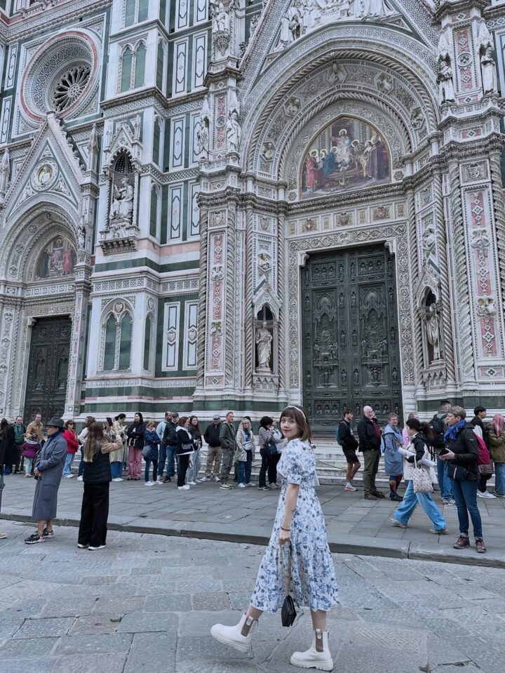 A woman in a floral dress walks outside a large ornate cathedral with people gathered around, capturing the essence of a perfect Florence Italy itinerary.