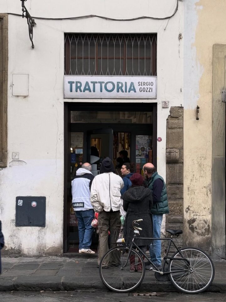 People stand outside Trattoria Sergio Gozzi, a spot known for authentic Florence food; a bicycle is parked by the entrance on a bustling city street.