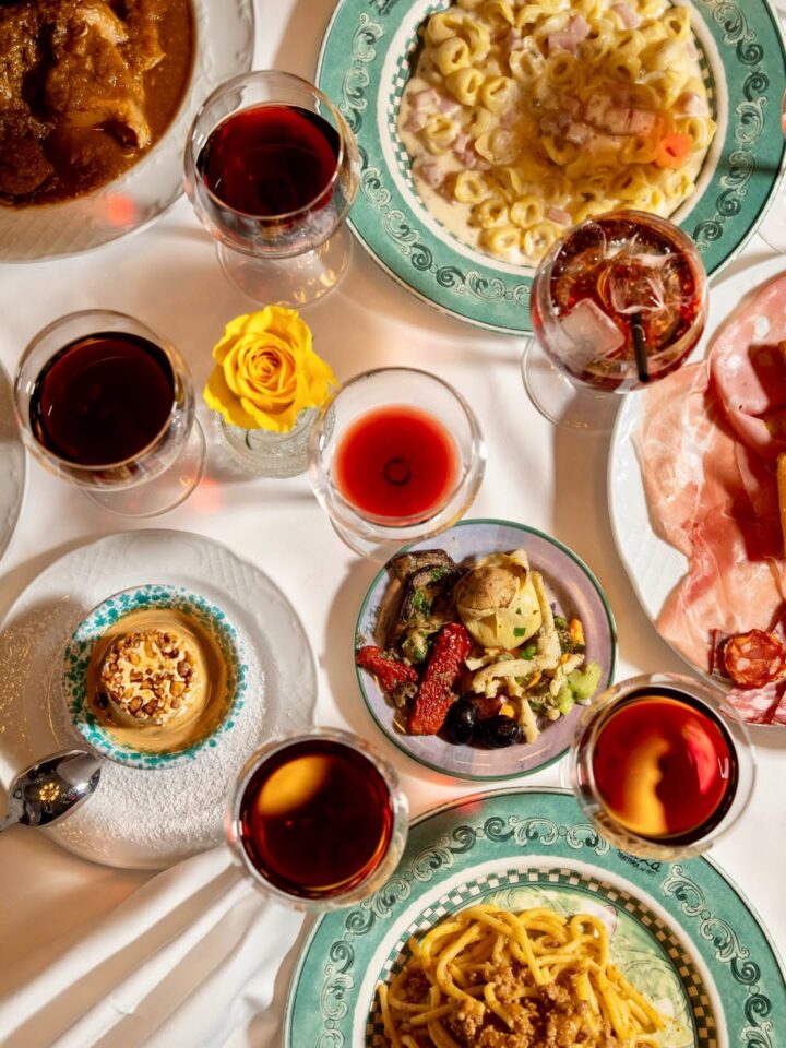 Italian dishes with pasta, antipasti, dessert, and glasses of red wine arranged on a table with a yellow rose&mdash;perfect inspiration for your Florence Italy itinerary.