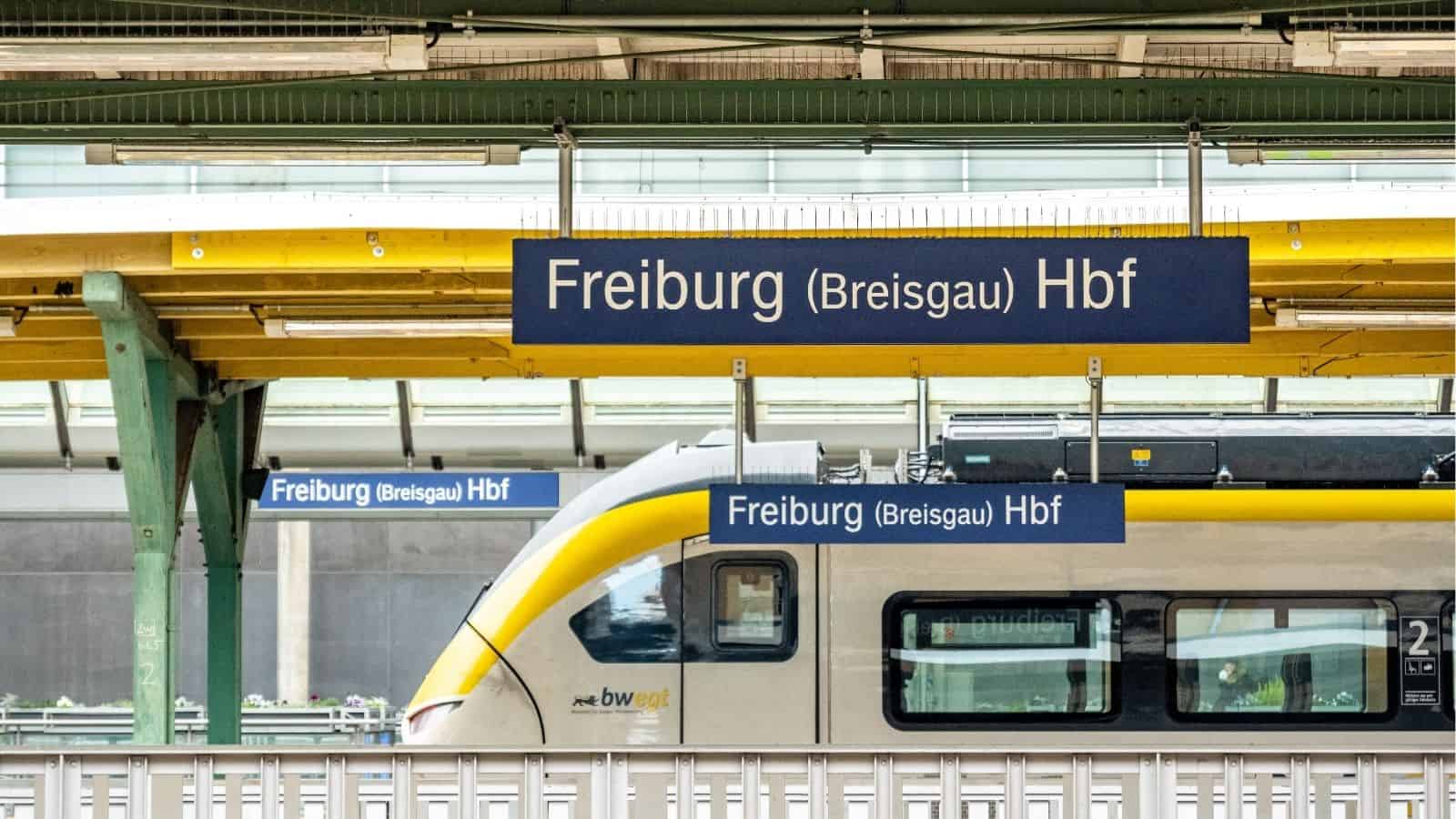A train at Freiburg (Breisgau) Hbf station with multiple blue station signs visible.