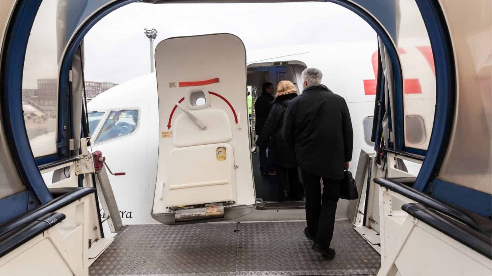 Passengers boarding an airplane through a jet bridge on a cloudy day.