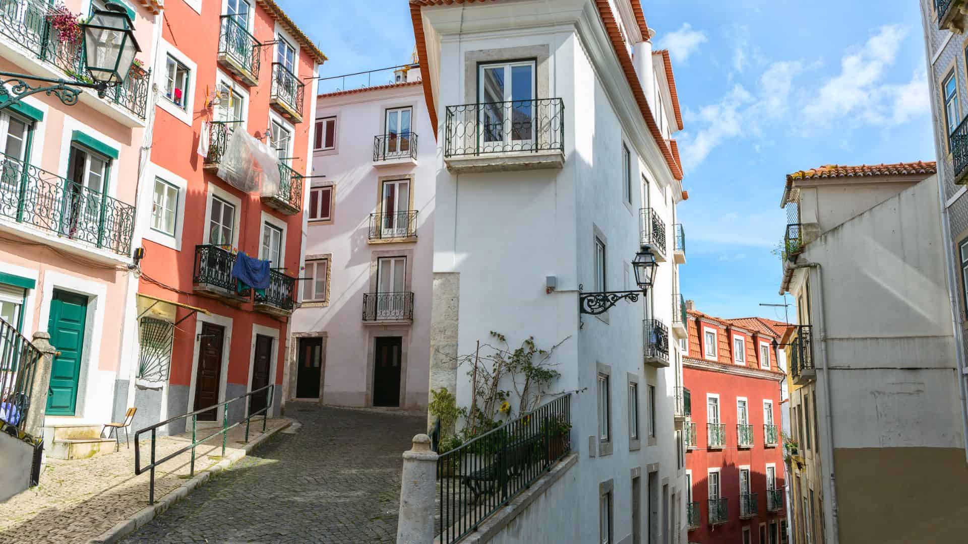 Narrow cobblestone street lined with colorful buildings and balconies under a clear blue sky.