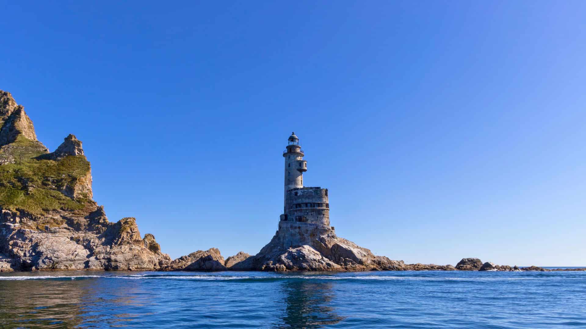 A lighthouse stands on a rocky island surrounded by blue sea under a clear sky.