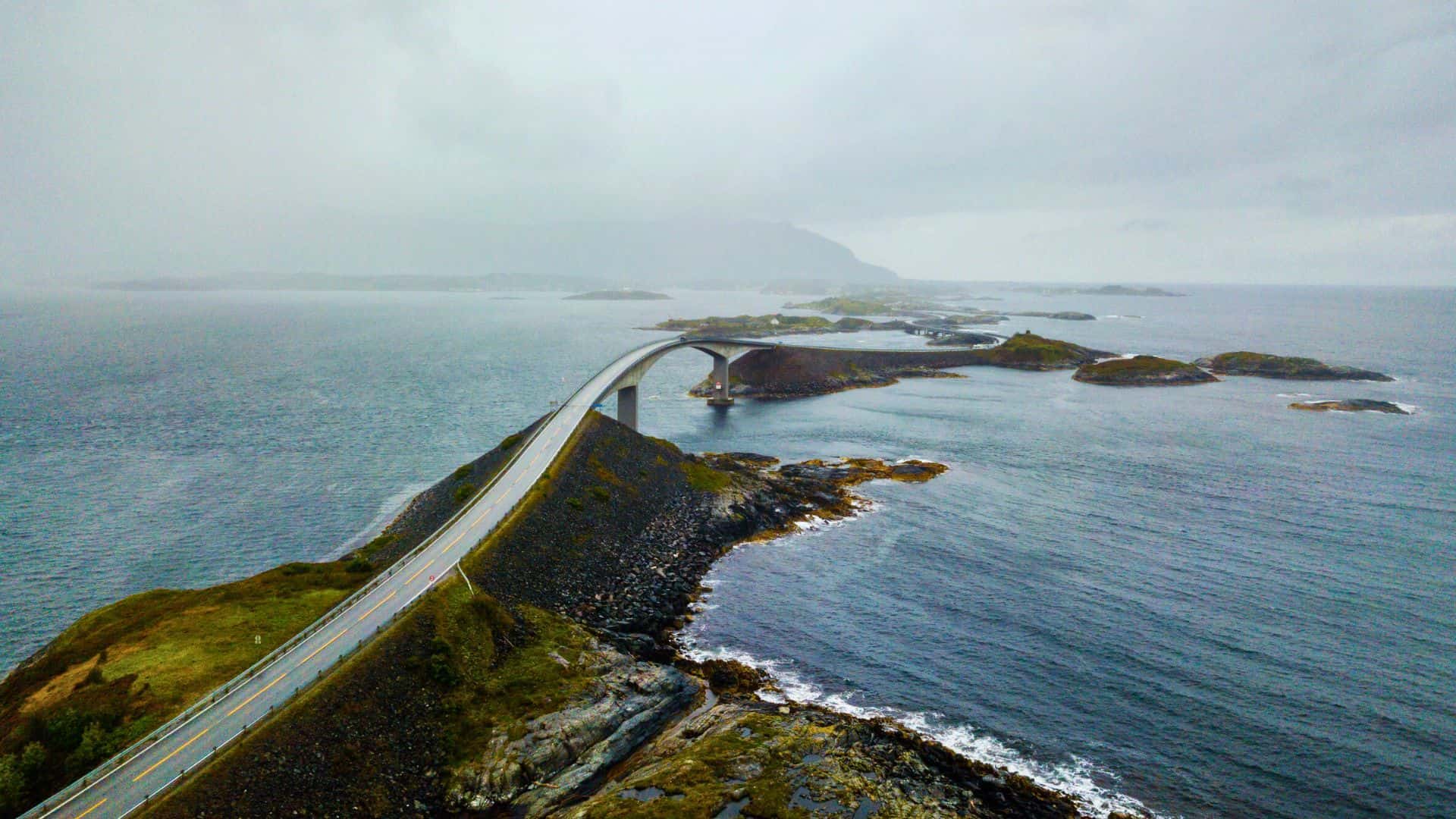 A curving bridge connects small islands over the sea on a cloudy, misty day.