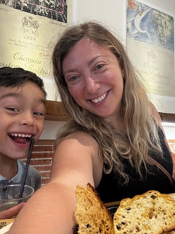 A woman and two children smile at a table with toasted bread in a cozy restaurant—a perfect snapshot for anyone wondering where to eat in Rome.