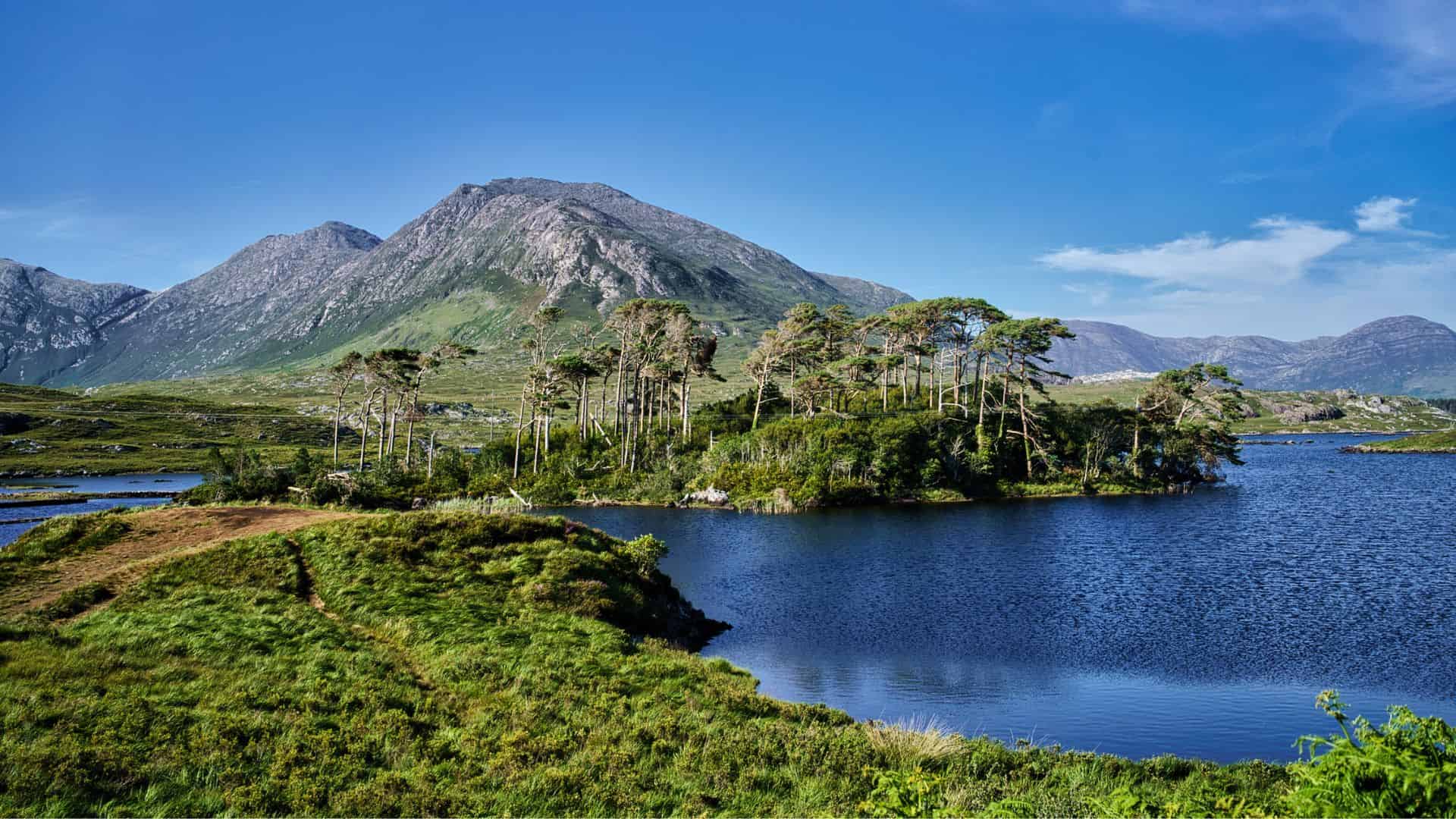 A lake with a small tree-covered island and mountains in the background under a blue sky.