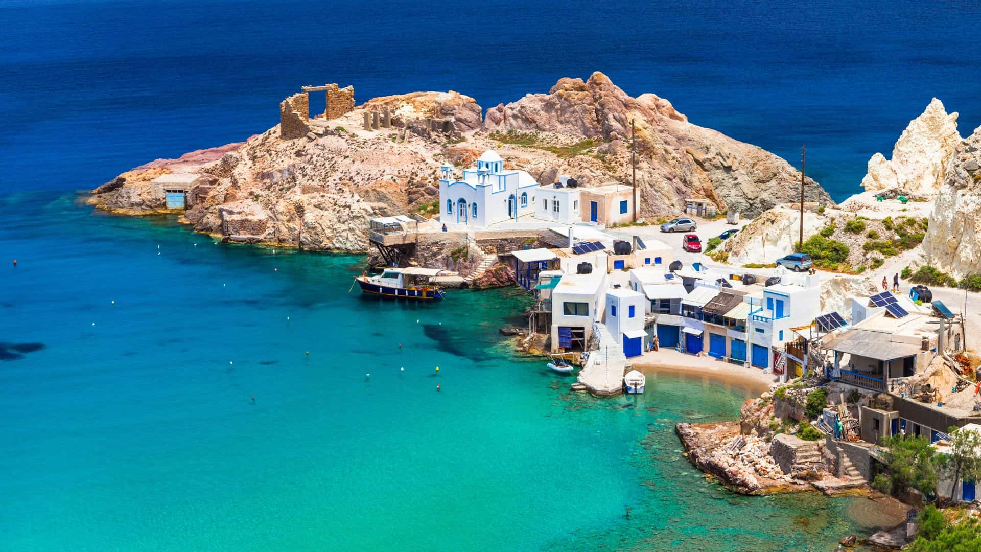 White and blue seaside buildings on a rocky coast with turquoise water and clear blue sky.
