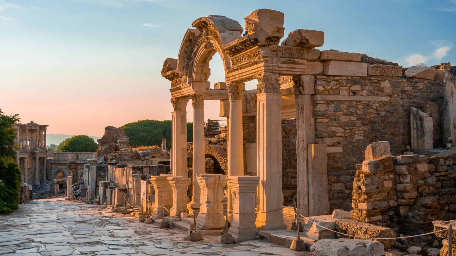 Ancient stone ruins with arches and columns illuminated by sunset, in an open archaeological site.