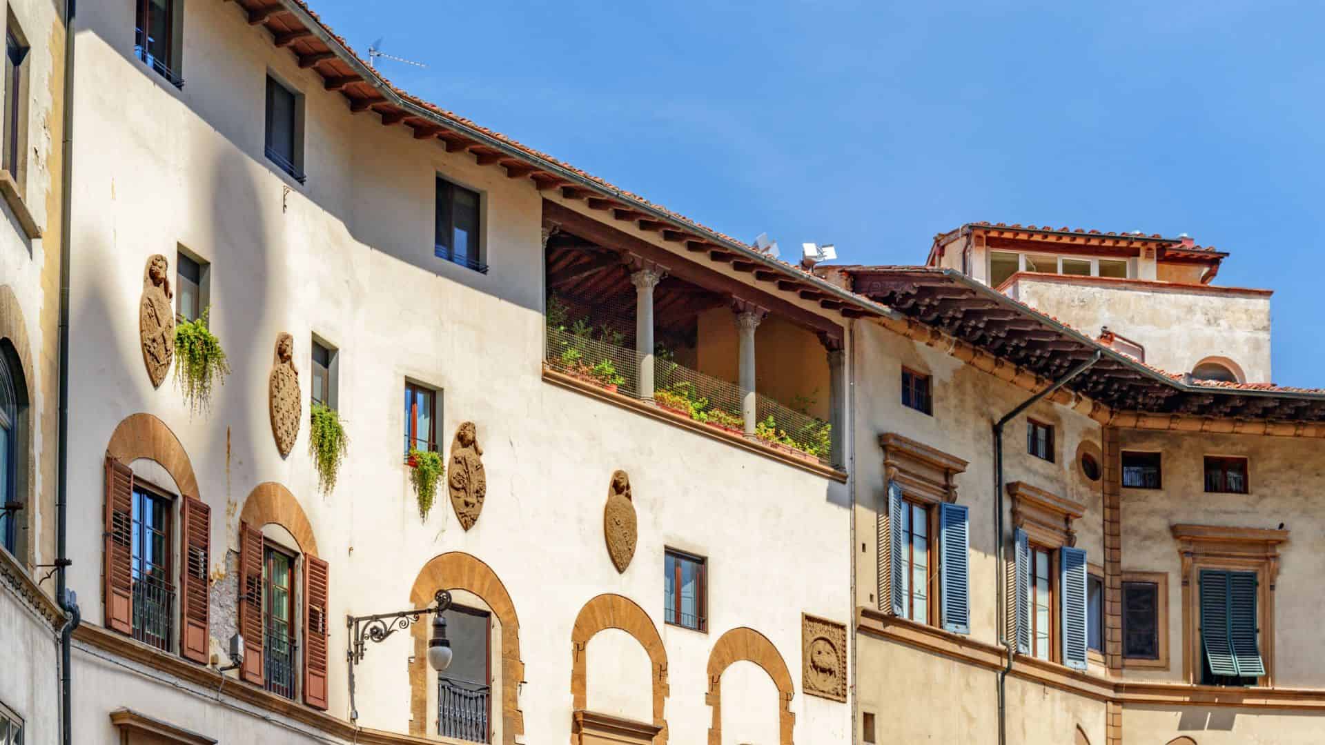 Old Italian building with arched windows, balconies, and decorative emblems against a clear blue sky.