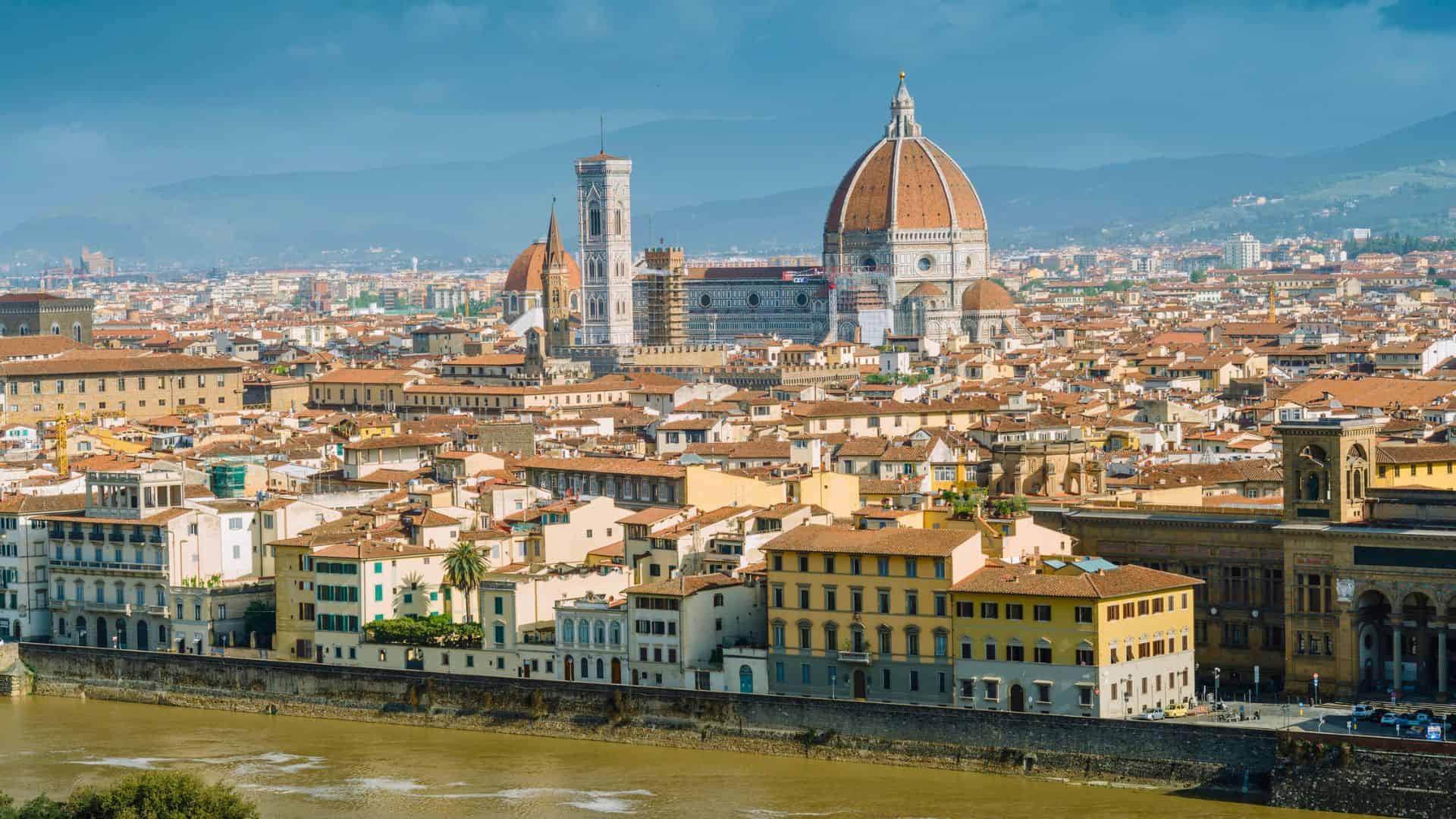 Panoramic view of Florence, Italy, with the Duomo cathedral and historic buildings along the Arno River.