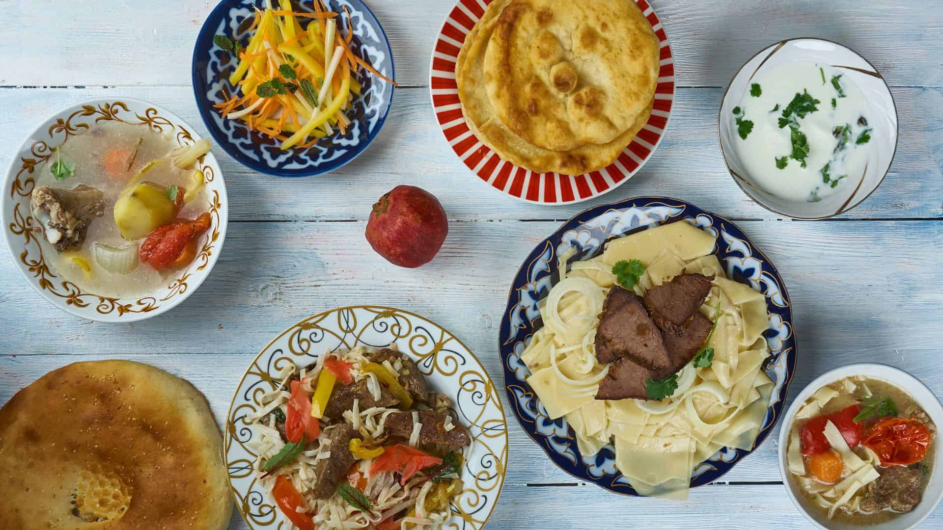 An assortment of Central Asian dishes, bread, and an apple arranged on a light wooden table.