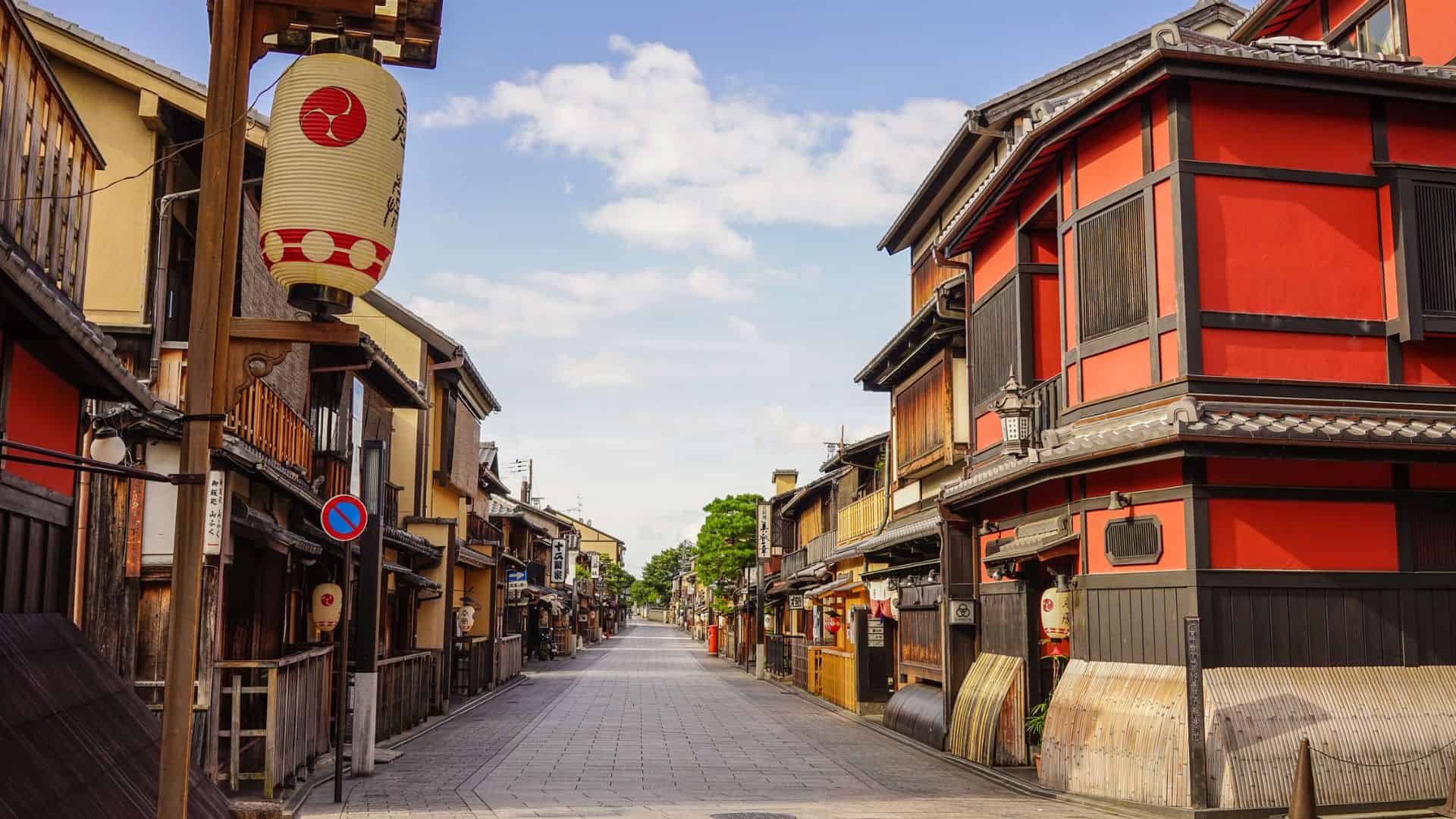 A quiet, traditional Japanese street with wooden buildings and a paper lantern under a blue sky.