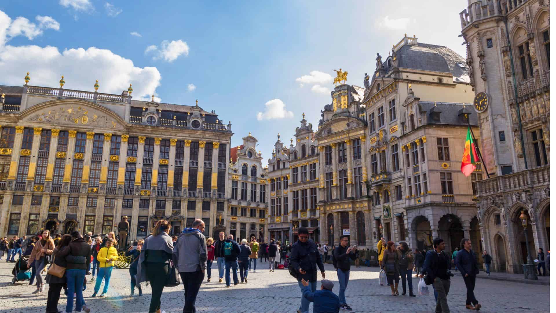 People walking in a sunny square surrounded by ornate, historic buildings in Brussels, Belgium.