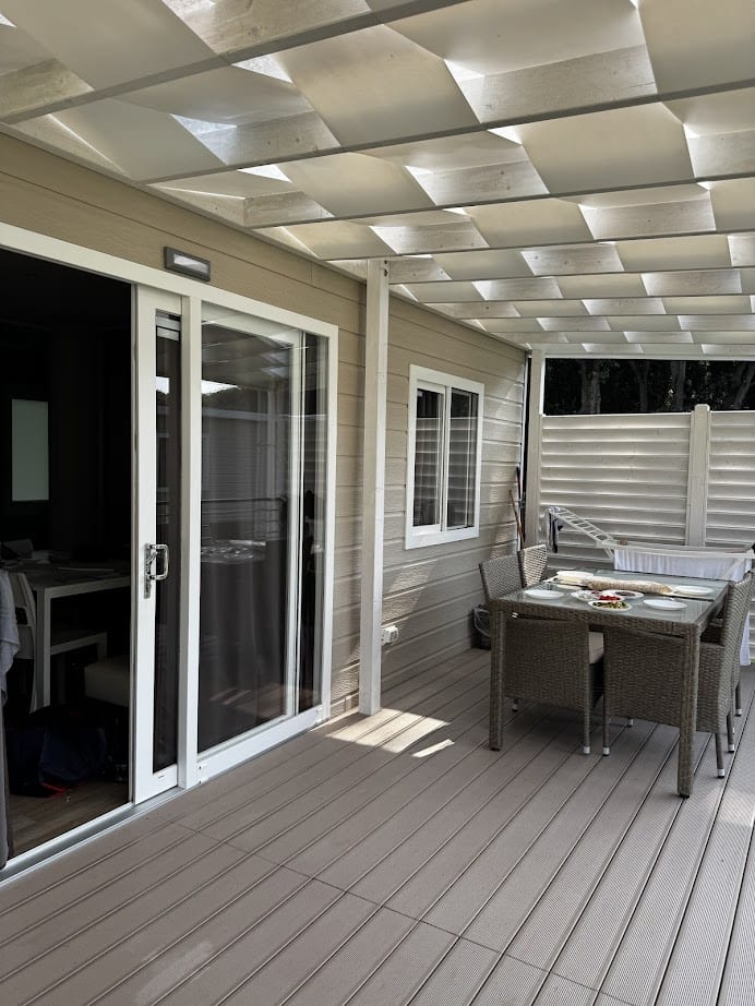 A covered patio with a table, chairs, sliding glass door, and beige wood paneling on the house exterior evokes the relaxed charm of homes near Parco della Gallinara.