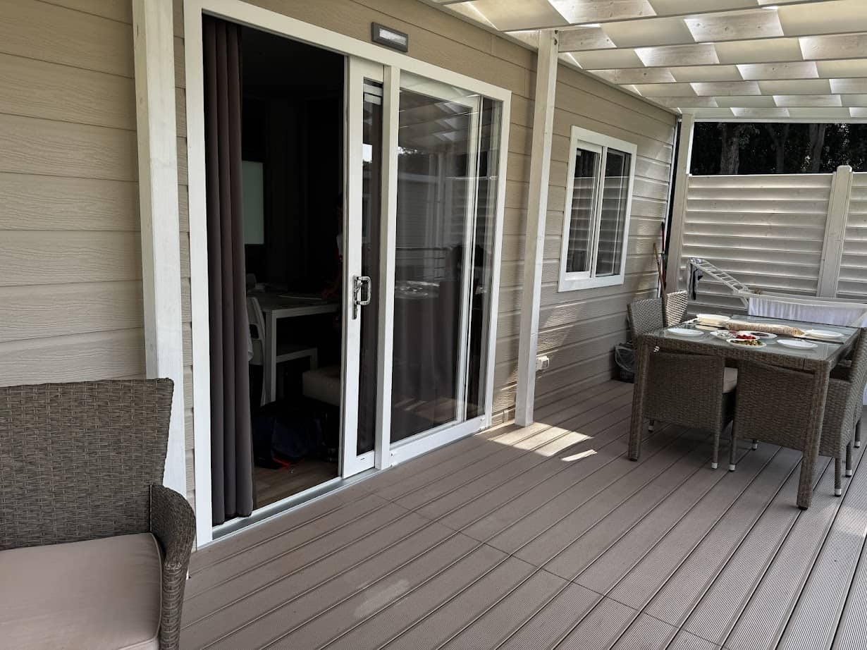 Covered patio with wicker chairs and dining table, next to sliding glass doors of a beige house, offering a relaxing spot reminiscent of parco della gallinara.