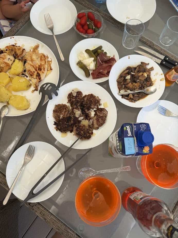 A table set at Parco della Gallinara with plates of fried potatoes, meat patties, mushrooms, cheese, pickles, and drinks.