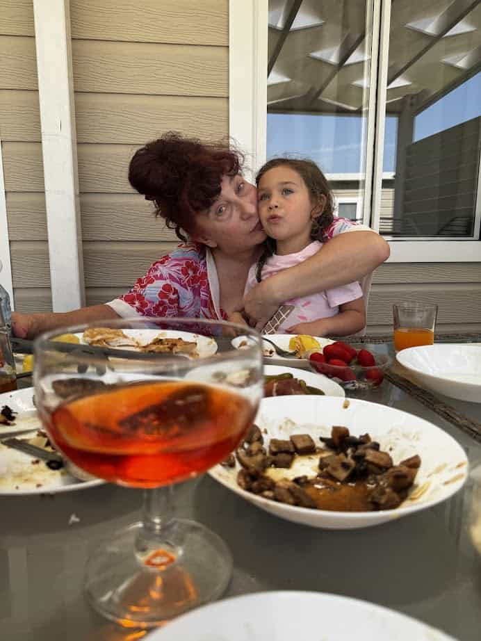Woman hugging a young girl at an outdoor table with food, drinks, and empty plates after a meal at Parco della Gallinara.