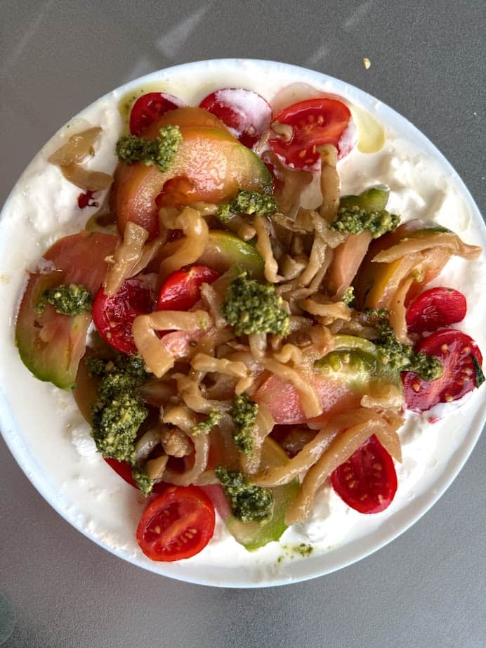 Burrata topped with sliced tomatoes, pesto, and caramelized onions on a white plate, inspired by the fresh flavors of Parco della Gallinara.