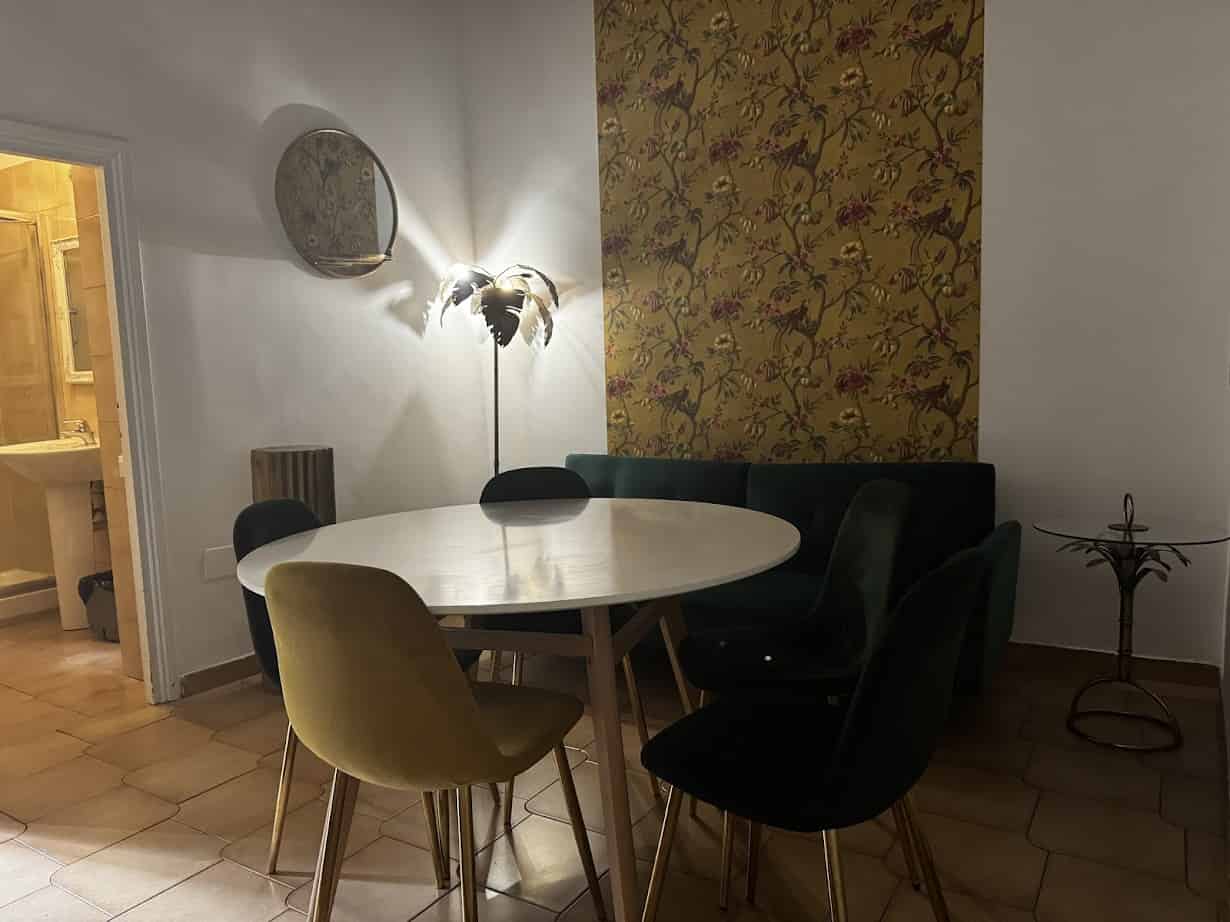 Round dining table with mixed velvet chairs, a floral wall, and a feather lamp in a dimly lit room—perfect for creating memories reminiscent of family adventures in Rome with kids.