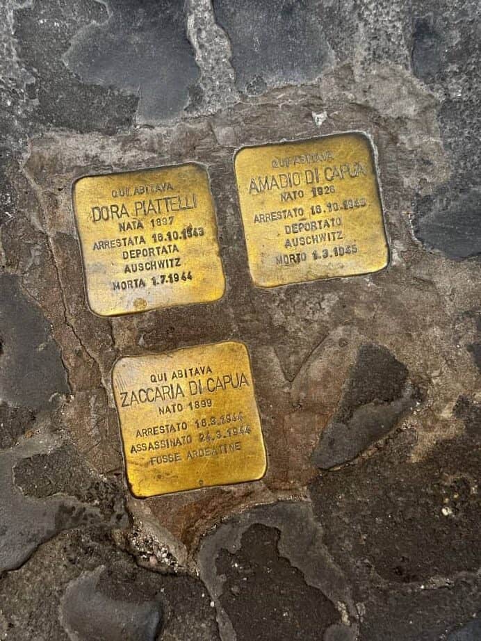 Three brass memorial plaques are embedded in a cobblestone sidewalk, offering a moment of reflection for families exploring Rome with kids on their vacation trip planner.