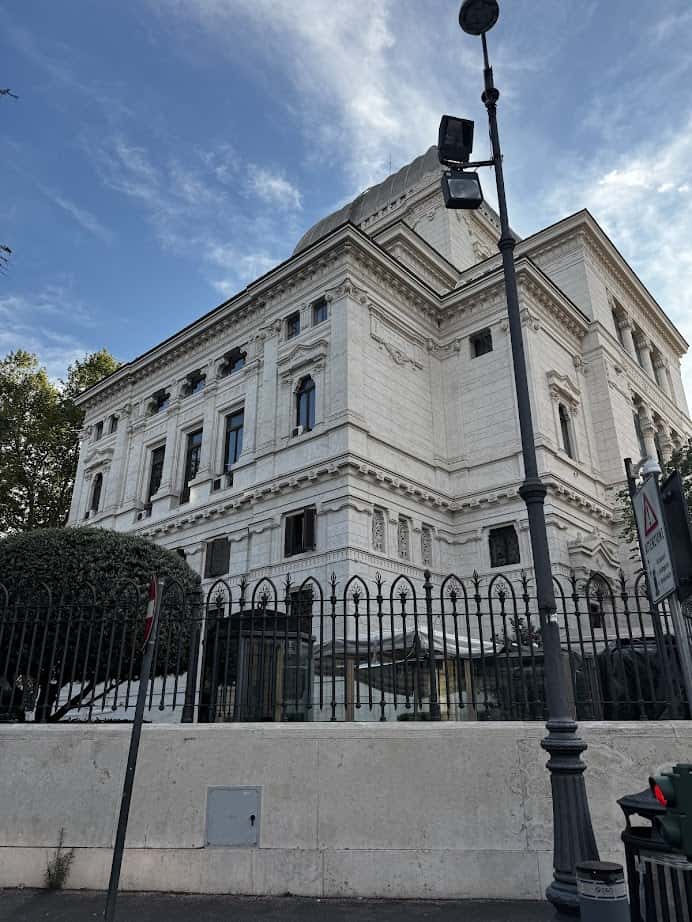 Large white stone building with decorative architecture, seen behind a black metal fence and streetlamp—perfect for your Family Itinerary when exploring Rome with Kids.