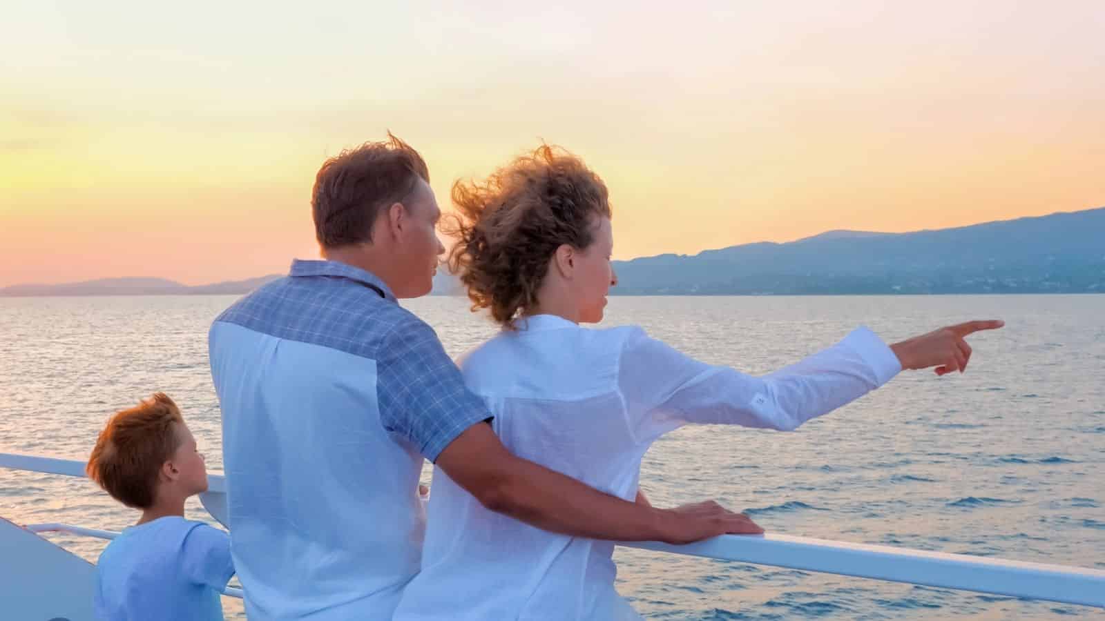 A family stands on a boat at sunset, looking out over the sea as a woman points toward the horizon.