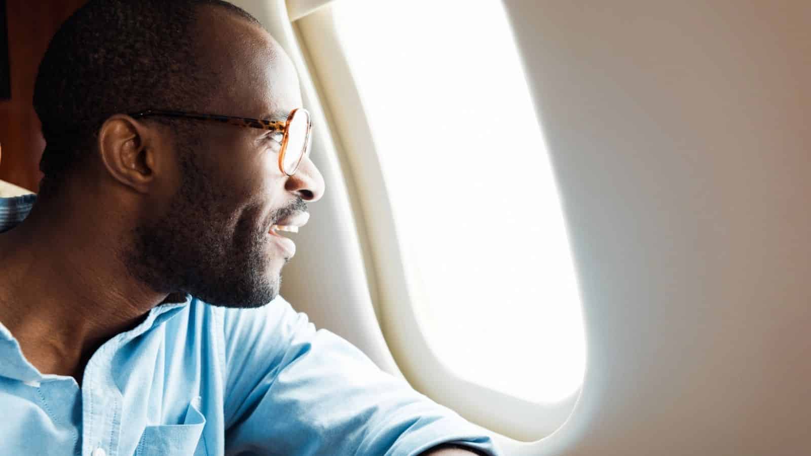 A man in glasses smiles while looking out the window of an airplane.