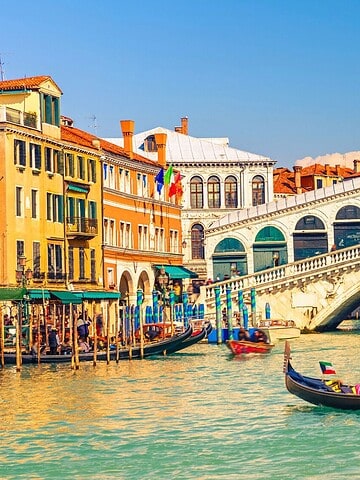 A gondola floats on a canal near the Rialto Bridge in Venice, Italy, on a sunny day.