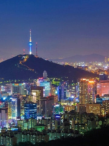 Seoul cityscape at night with Namsan Seoul Tower lit up and a full moon in the sky.
