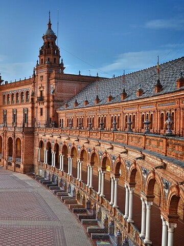 Plaza de España in Seville, Spain, at sunset with its canal, bridges, and grand Renaissance-style buildings.