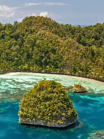 A sailboat is anchored in turquoise water near lush, green islands with dense tropical forest.