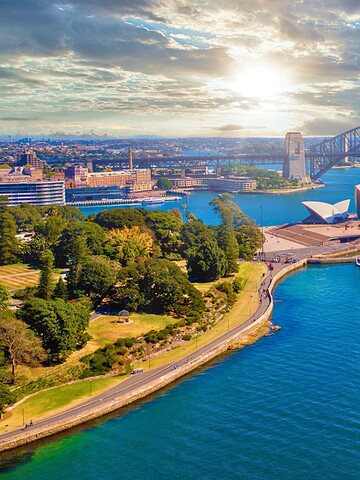 Aerial view of Sydney Opera House, Sydney Harbour Bridge, and a ferry on blue water at sunset.