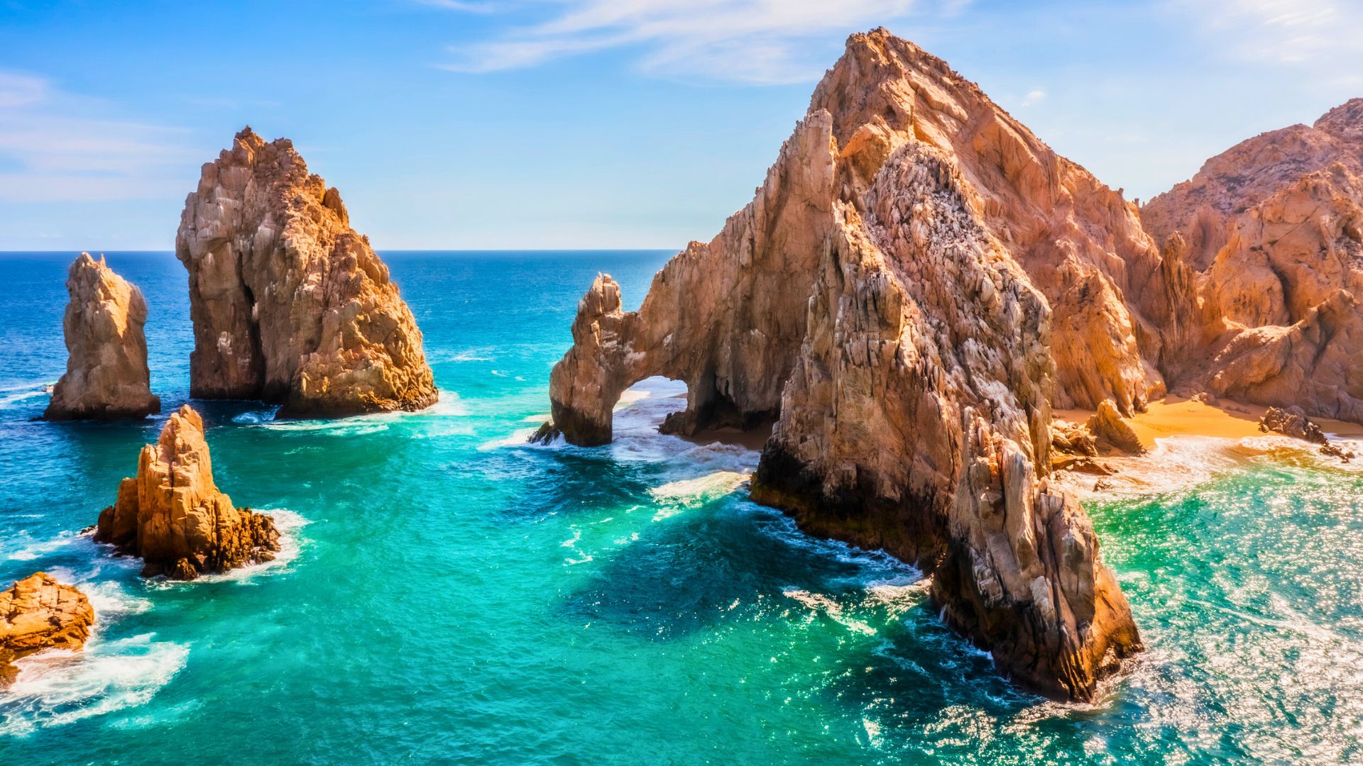 Vivid turquoise waters crashing against striking rock arches along the Mexican coastline.