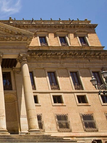 Neoclassical building facade with tall columns, ornate carvings, and wide stone steps under a blue sky.
