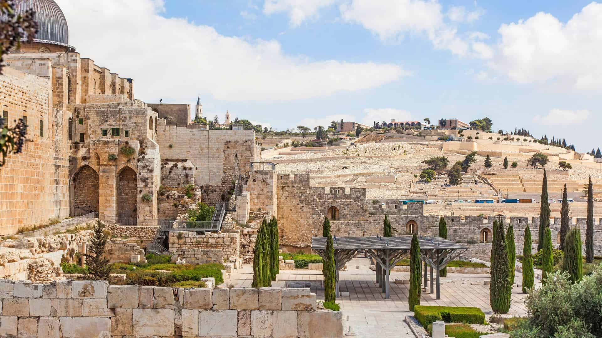 Ancient stone walls and gardens with distant hills under a partly cloudy sky in Jerusalem, Israel.