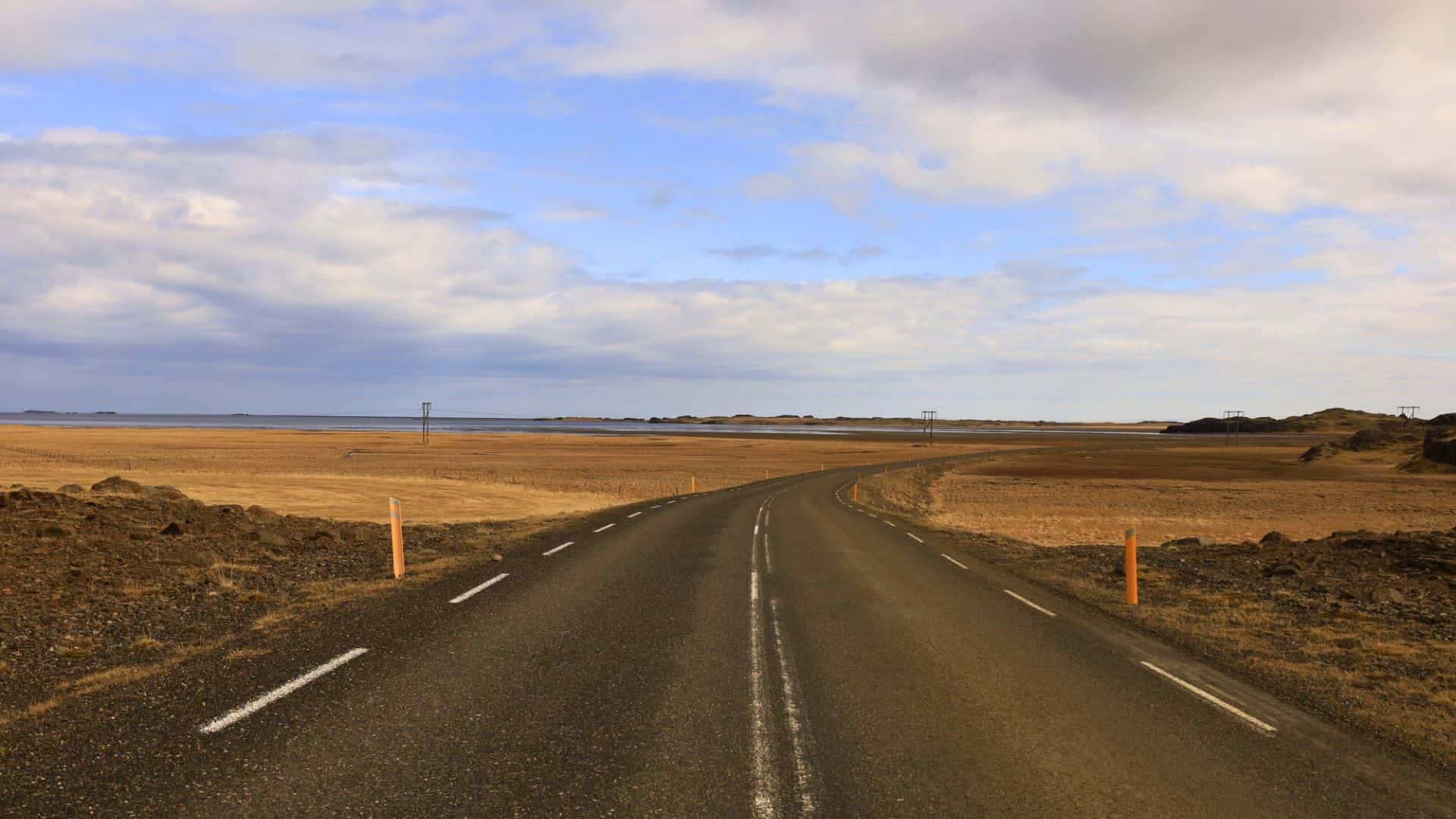 A winding road stretches through a flat, open landscape under a partly cloudy sky.