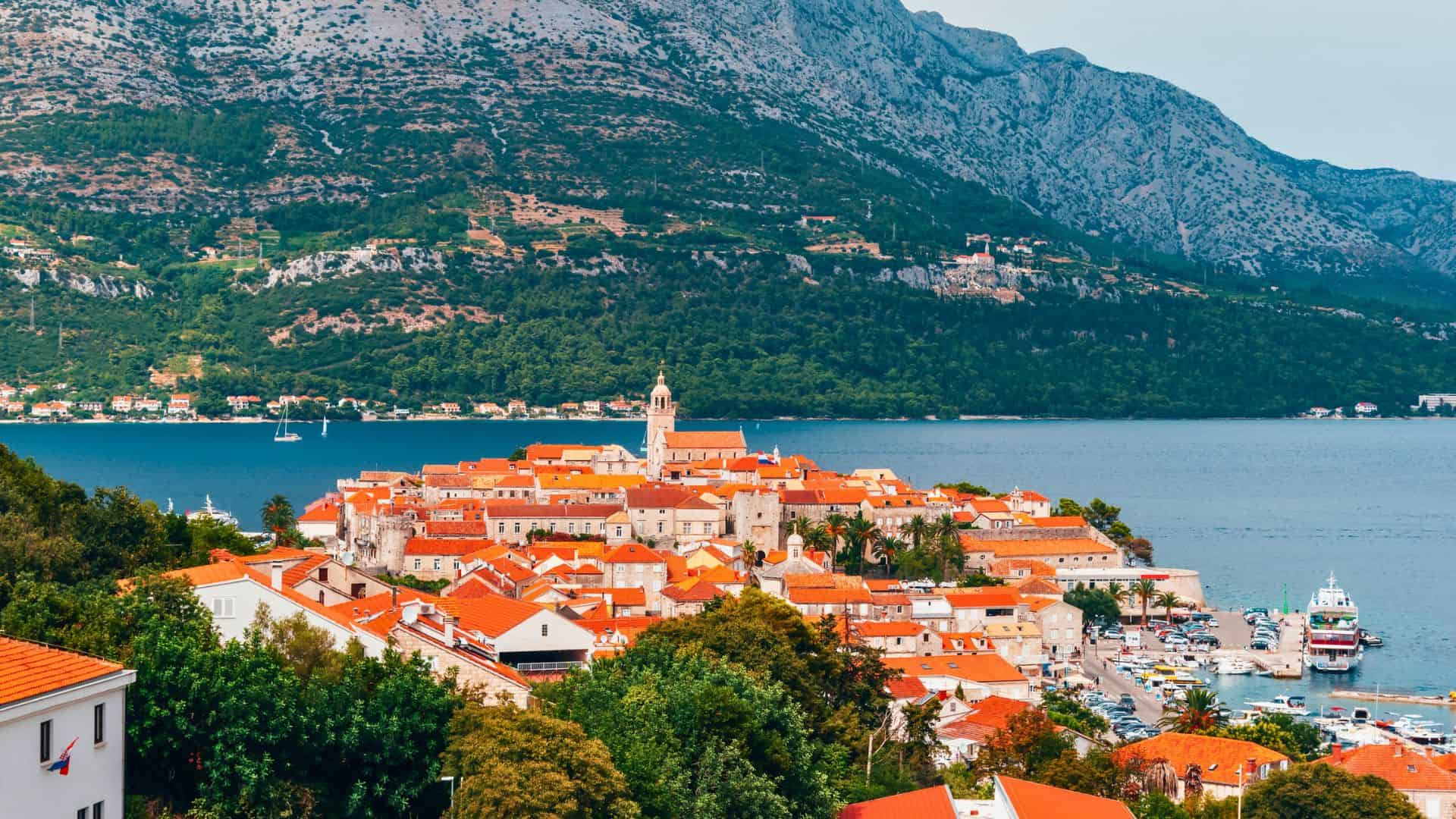 A city with red roofs and a body of water with mountains in the background.