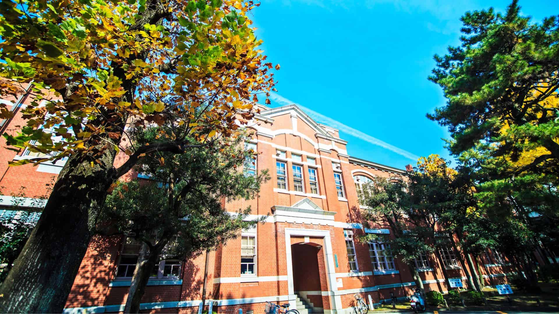 Red brick building surrounded by trees with autumn leaves under a bright blue sky.