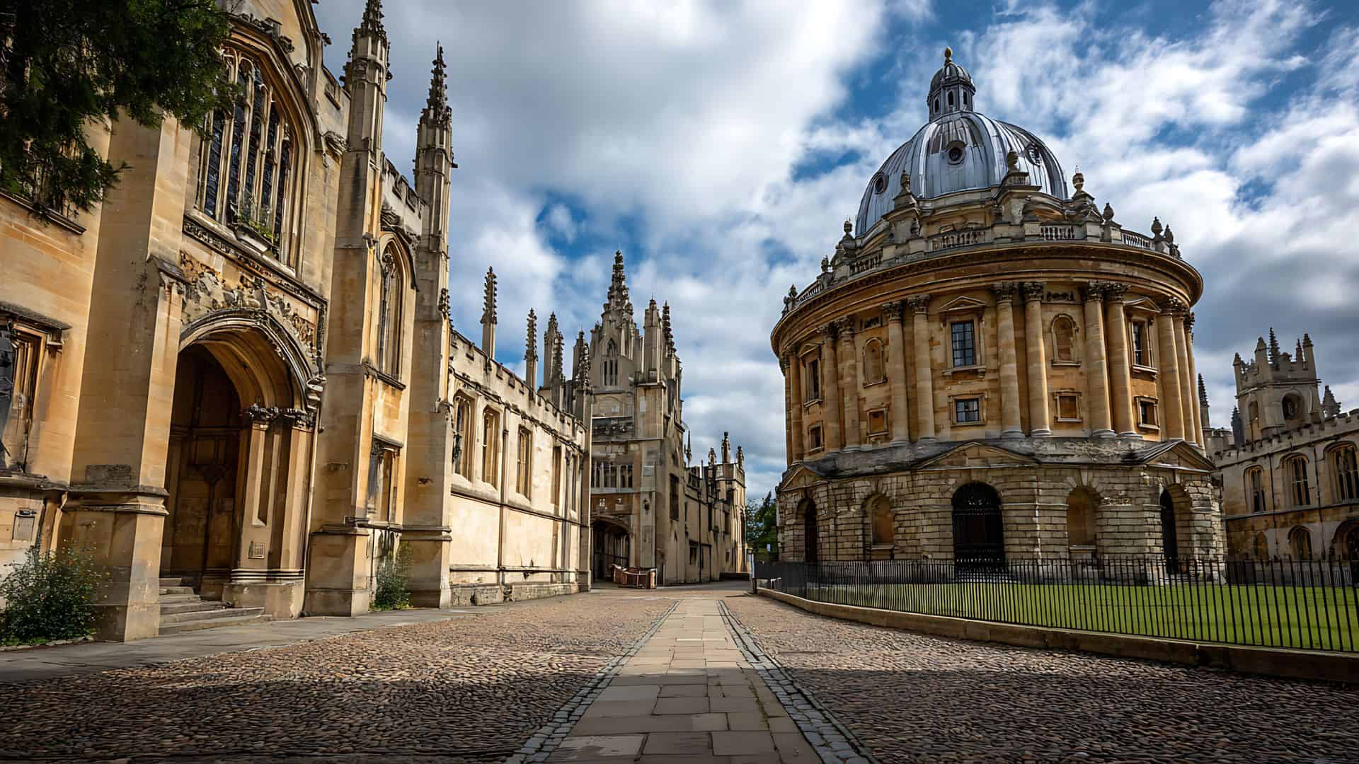 A cobblestone path between historic Oxford University buildings under a partly cloudy sky.