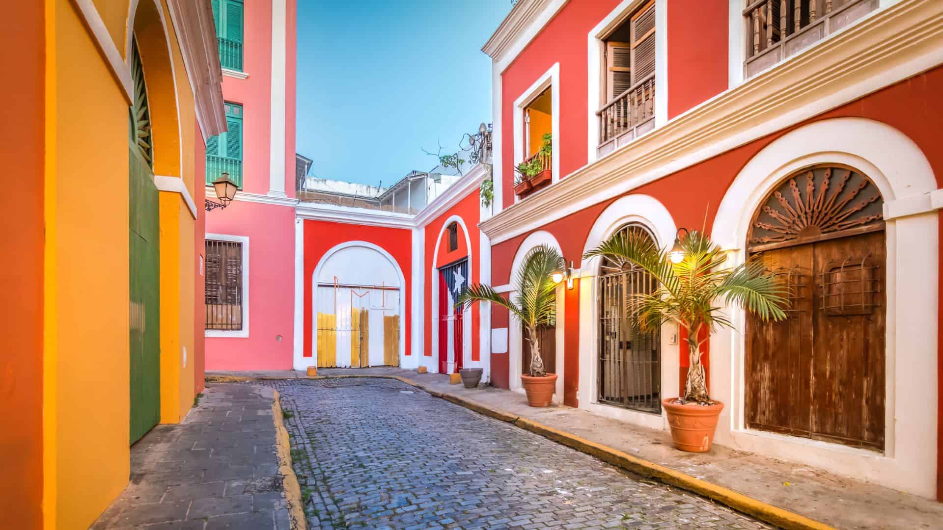 A colorful cobblestone street with vibrant buildings and potted palm trees in Old San Juan, Puerto Rico.